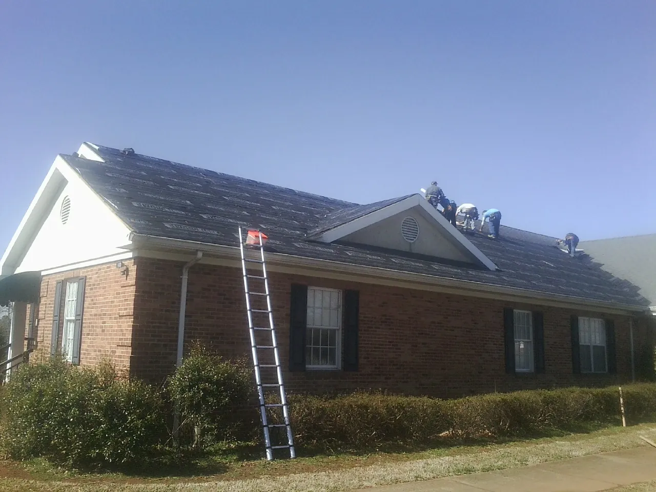 Crew tearing shingles off a brick ranch roof with a ladder set — Emergency Roof Repair work by our crew in Bentonville