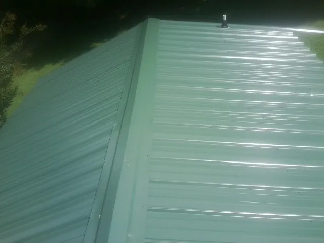 New green metal panels meeting at the ridge of a roof — Flat Roof Repair work by our crew in Bentonville