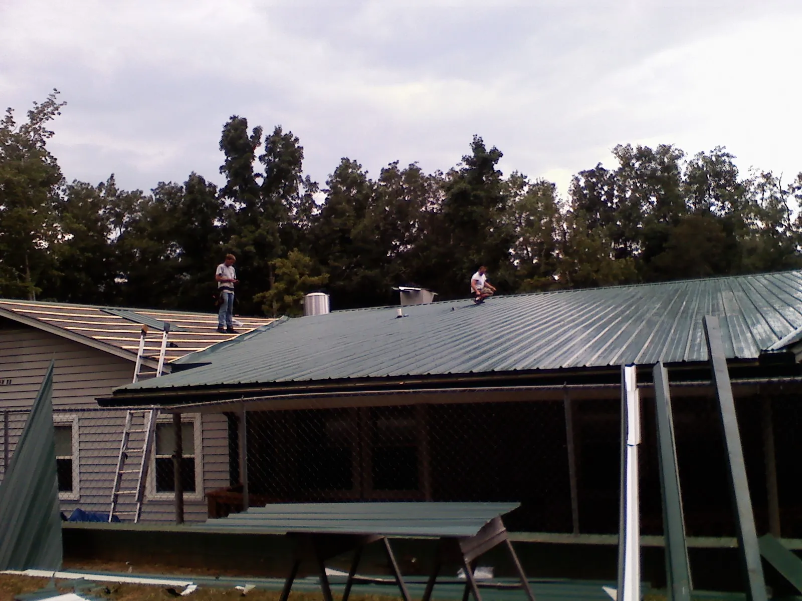 Two roofers installing green metal panels above a covered porch in Bentonville
