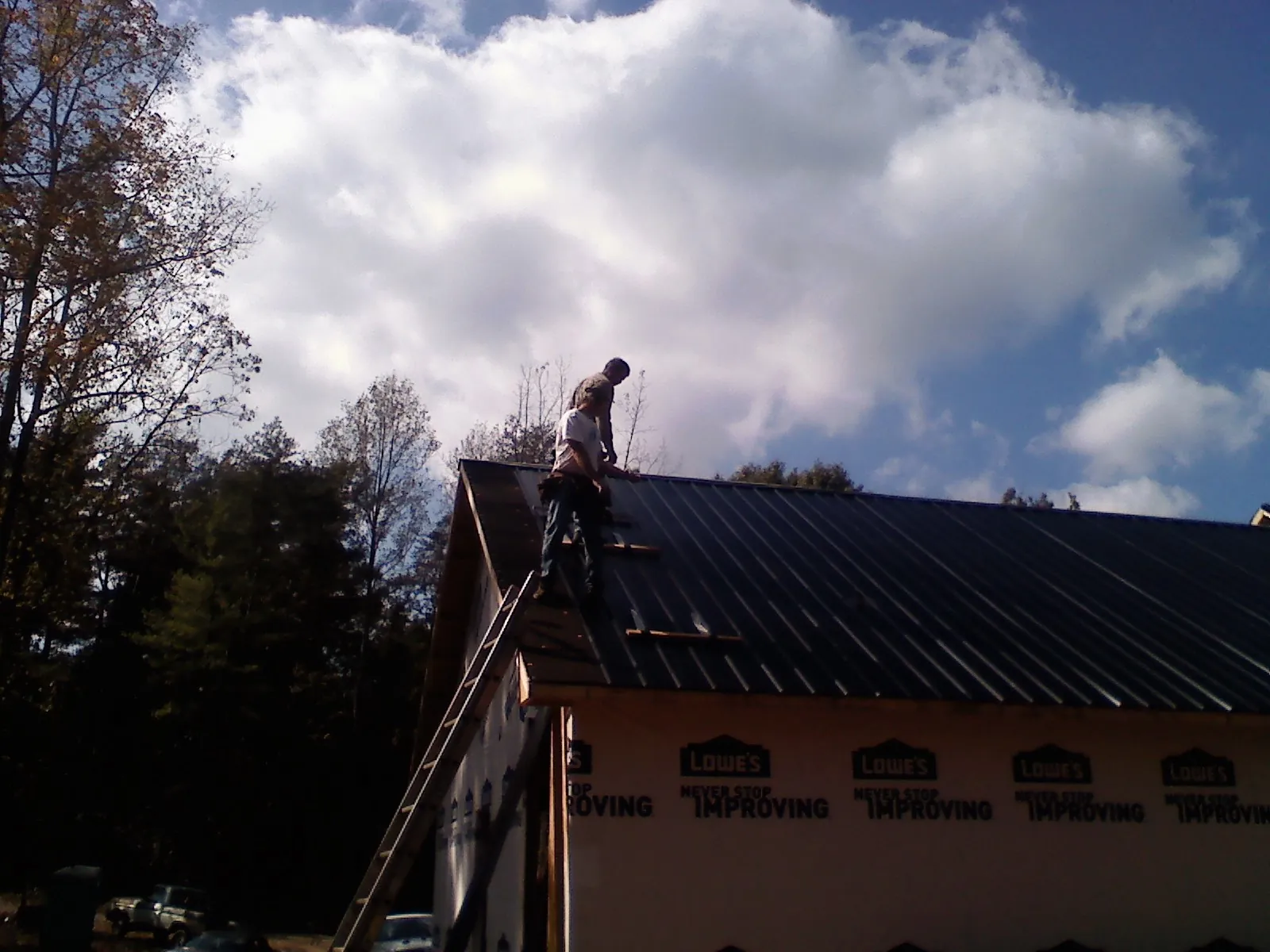 Roofer fastening dark metal panels high against a cloudy sky, from a Roof Inspection job in Bentonville
