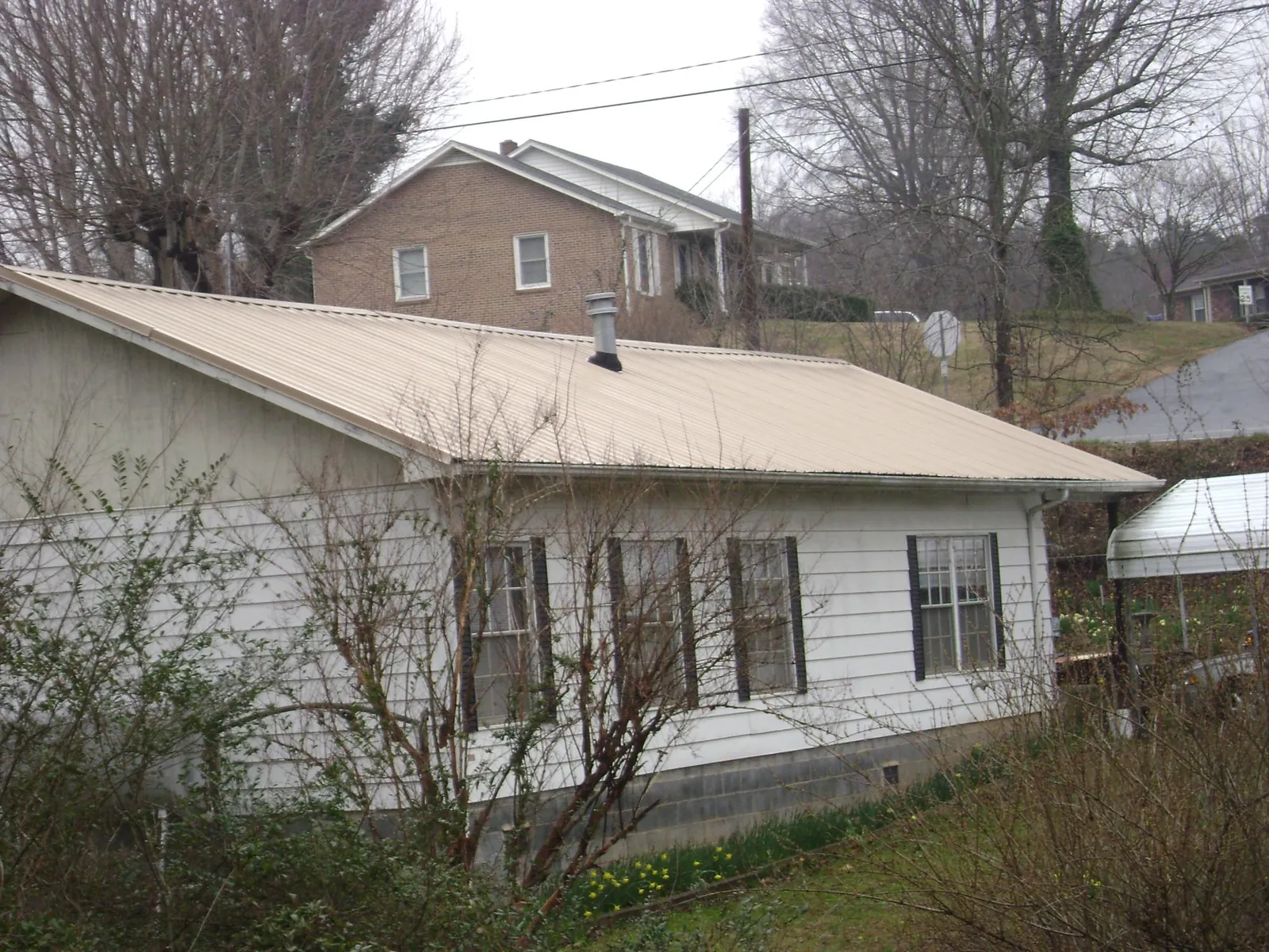 Tan metal roof on a white sided house set into a hillside — Commercial Roofing by Roofing Brothers in Bentonville